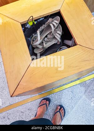 Frau wirft ihre alten Flip-Flops Sandalen in eine Mülltonne. Stockfoto