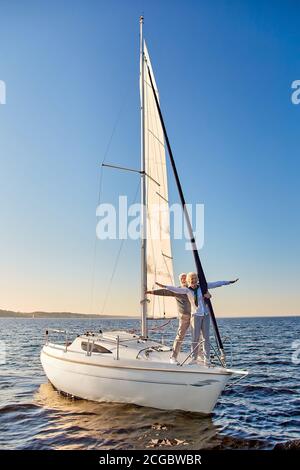 Glückliches Seniorenpaar, das sich gegen den Himmel streckt, den Horizont anschaut und eine herrliche Aussicht genießt, auf der Seite eines Segelbootes oder einer Yacht steht Stockfoto