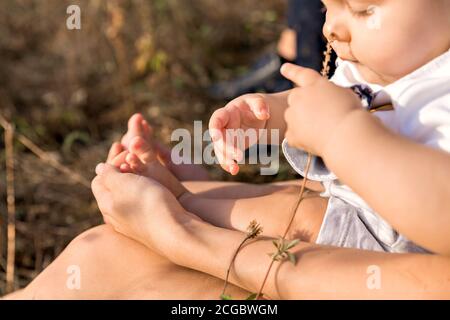 Baby auf einem Spaziergang mit seiner Mutter an einem warmen sonnigen Tag. Die kleine dicke Hand des Babys in den Händen meiner Mutter. Konzentrieren Sie sich auf Ihre Finger. Stockfoto