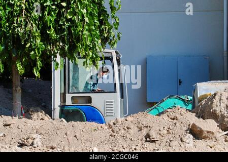 Bauarbeiter mit Maske, die während der Covid-19-Ära den Bulldozer auf der Baustelle bediente. Covid-19-Inhalt Stockfoto