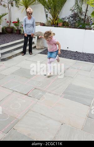 Eine Großmutter lehrt ihre Enkelin das traditionelle Spiel von hopscotch. Stockfoto