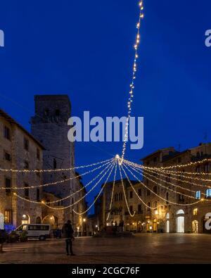 Vertikale Ansicht der Piazza della Cisterna Platz, historisches Zentrum von San Gimignano, Siena, Italien, mit den Lichtern der Dämmerung in der blauen Stunde Stockfoto