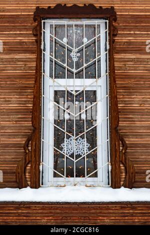 Ein vergittertes Fenster in einem alten Holzhaus. Winter. Stockfoto