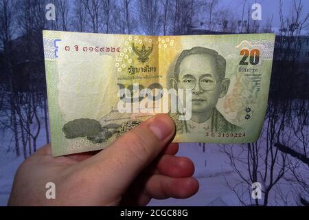 In der Hand von 20 thailändischen Baht vor dem Hintergrund einer dunklen Stadt in Sibirien. Blick von vorne. Stockfoto