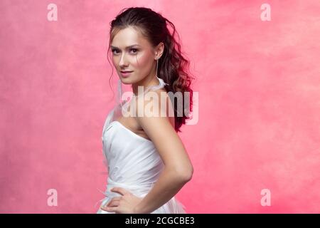 Porträt einer jungen schönen Frau in eleganten weißen, strukturierten rosa Hintergrund. Die Braut mit einem leichten und stilvollen Styling. Schöne junge Brünette. Stockfoto