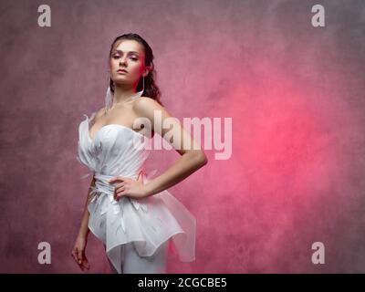 Porträt einer jungen schönen Frau in einem eleganten weißen Anzug, strukturierte rosa Hintergrund. Braut in einem modernen Stil Stockfoto