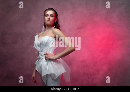 Porträt einer jungen schönen Frau in einem eleganten weißen Anzug, strukturierte rosa Hintergrund. Braut in einem modernen Stil Stockfoto