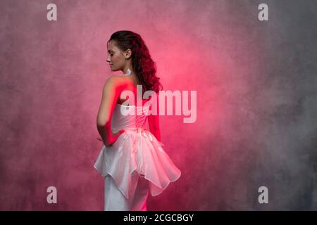 Porträt einer jungen schönen Frau in einem eleganten weißen Anzug, strukturierte rosa Hintergrund. Braut in einem modernen Stil Stockfoto