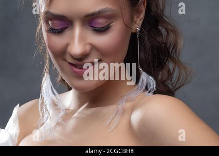Stilvolle und elegante Braut in einem modernen Anzug, Porträt. Make-up in rosa Farbtönen, Ohrhänger mit weißen Federn. Stockfoto