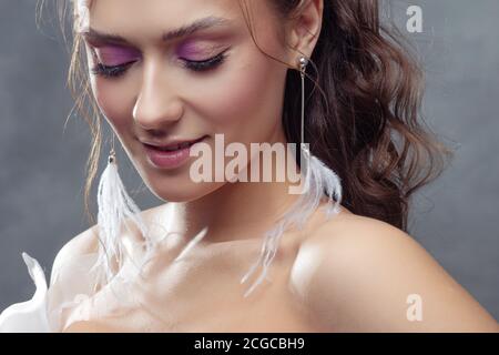 Stilvolle und elegante Braut in einem modernen Anzug, Porträt. Make-up in rosa Farbtönen, Ohrhänger mit weißen Federn. Stockfoto