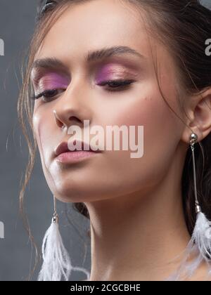 Stilvolle und elegante Braut in einem modernen Anzug, Porträt. Make-up in rosa Farbtönen, Ohrhänger mit weißen Federn. Stockfoto
