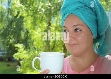 Junge Frau trinkt Kaffee auf dem Balkon auf dem Hintergrund der Natur. Glückliche Frau am Morgen Stockfoto