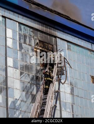 Russland, Kaluga - 08. SEPTEMBER 2020: Ein Team von Feuerwehrleuten in Schutzanzügen und Helmen auf der Treppe Löschen eines Feuers in einem Gebäude mit einem Br Stockfoto