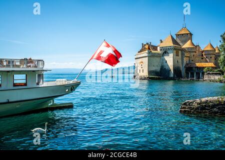 Schweizer Flagge auf der Rückseite eines Bootes und Chillon Schloss mit sonnigem blauen Himmel in der Waadtländer Schweiz Stockfoto