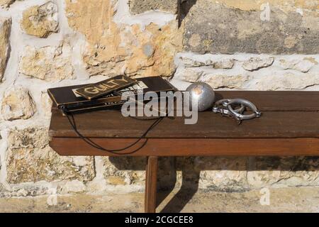 Fremantle, Western Australia - August, 2020: Schuldige Schild, metallische Handschellen und Mäntelchen auf einer Holzbank auf einem gelben Kalkstein Hintergrund in Stockfoto