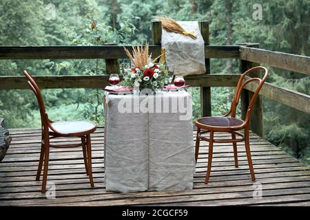 Ein Ort für ein romantisches Date im Wald. Der Tisch ist mit frischen Blumen geschmückt. Desprts, Kuchen und Sekt. Tischdecke aus rustikalem Leinen. Wein Stockfoto