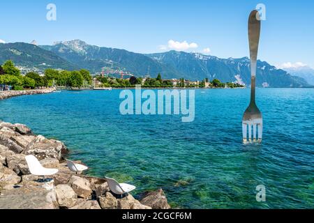 Leere Stühle auf Felsen am Ufer des Genfer Sees und Weltgrößte Gabel in Vevey Schweiz Stockfoto