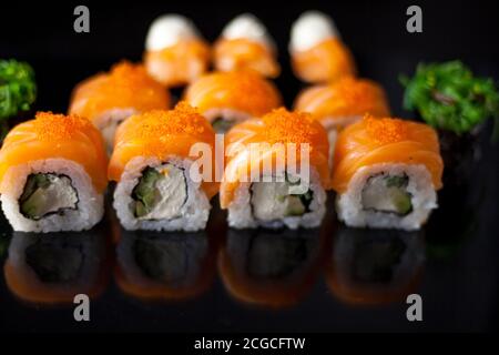 Sushi-Set mit Lachs. Sushi-Rolle Philadelphia mit rotem Fisch, Lachs, rotem Kaviar. Rollen Sie mit weicher Avocado und Frischkäse unter einer Schicht Massago Kaviar Stockfoto