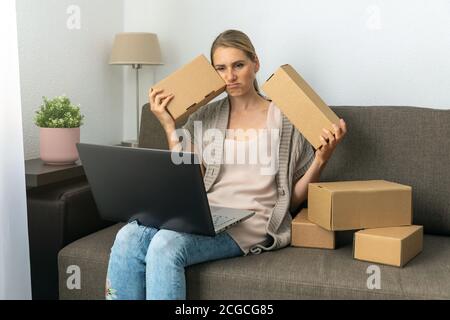 Erschöpft müde Frau kleines Handwerk Unternehmer sitzen auf Couch mit Boxen und Laptop. Verarbeitet und bereitet Sendungen aus dem Online-Shop Stockfoto