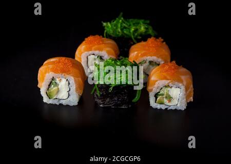 Sushi-Set mit Lachs. Sushi-Rolle Philadelphia mit rotem Fisch, Lachs, rotem Kaviar. Rollen Sie mit weicher Avocado und Frischkäse unter einer Schicht Massago Kaviar Stockfoto