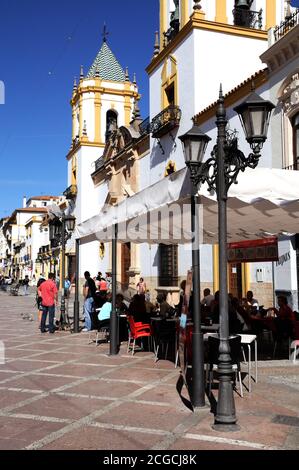 Touristen entspannen im Straßencafés in der Plaza Socorro mit dem Pfarrlichen Zentrum (centro parroquial) nach hinten, Ronda, Spanien. Stockfoto