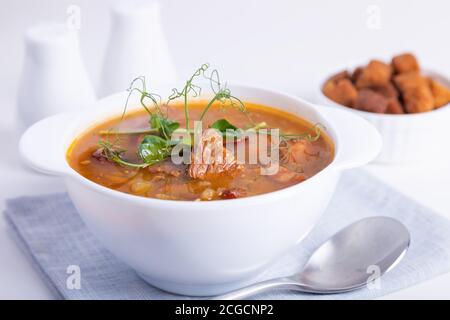 PEA-Suppe mit Fleisch, Räucherwurst, Erbsensprossen und Croutons. Traditionelles russisches Gericht. Wohnküche. Nahaufnahme, selektiver Fokus. Stockfoto