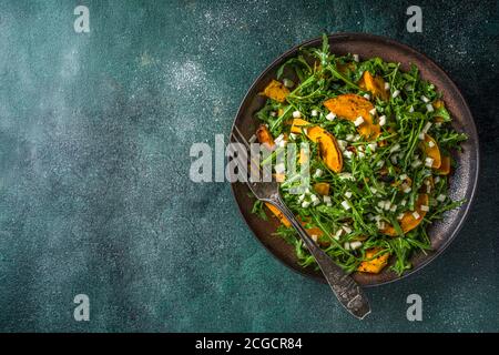 Hausgemachter Kürbissalat mit gegrillten Kürbisscheiben, Rucola und Käse. Herbst Kürbis Salat Rezept, dunklen Hintergrund kopieren Raum Stockfoto