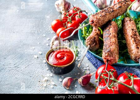 Shish Kebab auf Spieße, aus Hackfleisch Rindfleisch. Lula Kebab, traditionelle kaukasische Rezept. Auf blauem Betonboden, mit Saucen, Tomaten und Veggi Stockfoto