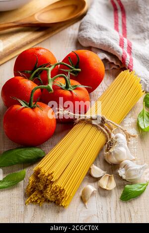 Rohe Spaghetti-Pasta in einem Bündel mit frischen Weintomaten, Knoblauch und Basilikum auf einem rustikalen Holztisch gebunden Stockfoto