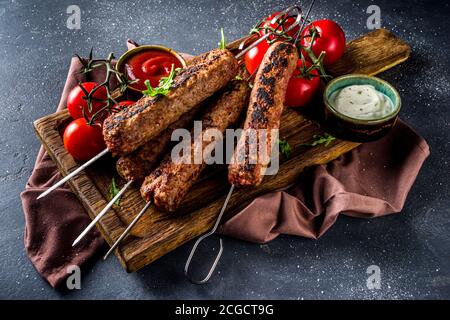 Shish Kebab auf Spieße, aus Hackfleisch Rindfleisch. Lula Kebab, traditionelle kaukasische Rezept. Auf schwarzem Betonboden, mit Saucen, Tomaten und Veggi Stockfoto