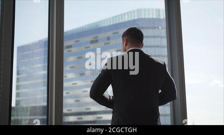 Erfolgreicher Geschäftsmann in seinem Büro. Der Geschäftsmann nähert sich selbstbewusst dem Fenster. Stockfoto