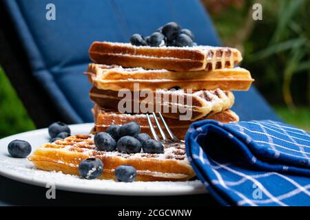 Original belgische Waffeln gerade gebacken und als Stapel serviert Mit frischen Heidelbeeren auf einem weißen Teller draußen Stockfoto