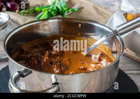 Geschmortes Schweinefleisch in cremiger Sauce in einem Topf serviert Auf einem rustikalen Tisch mit Schöpfkelle Stockfoto