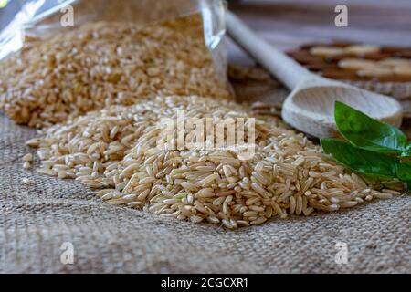 Roher und ungekockter brauner Reis mit einem Holzlöffel auf Eine Jute-Textur Stockfoto