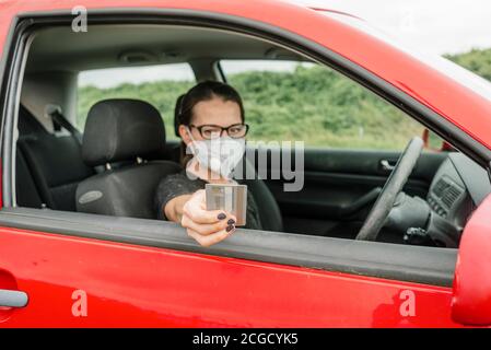 Frau in einem roten Auto trägt eine schützende Gesichtsmaske Gegen Covid, die mit ihrer Kreditkarte bezahlt, ohne die zu verlassen Auto Stockfoto