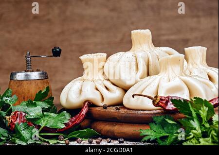 Set von gekochten saftigen hausgemachten Khinkali Knödel mit Petersilienblättern verziert, rote heiße Chilli auf Holz Hintergrund Stockfoto