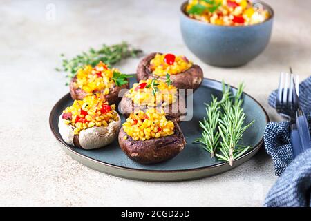 Gebackene gefüllte portobello-Pilze mit Bulgur-Pilaf und gehacktem Gemüse. Leckeres und nahrhaftes vegetarisches Gericht. Steinhintergrund. Stockfoto