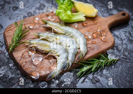 Frische Garnelen auf Holz Schneidebrett mit Rosmarin Zutaten Kraut Und Gewürze zum Kochen von Meeresfrüchten / rohen Garnelen Garnelen Eis gefroren bei den Meeresfrüchten r Stockfoto