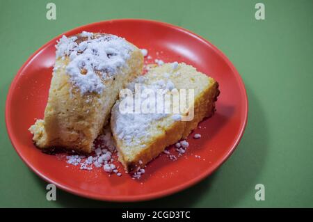 Servieren auf rotem Teller hausgemachter Käsekuchen, Portionieren auf rotem Teller, auf grünem Hintergrund (selektiver Fokus; Nahaufnahme) Stockfoto