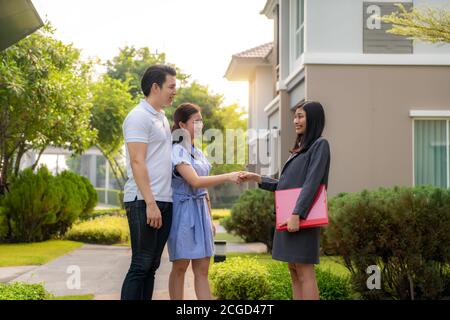 Glückliches asiatisches Paar sucht nach ihrem neuen Haus und schüttelt nach einem Deal die Hände beim Immobilienmakler. Junges Paar händernde Immobilienmakler nach Stockfoto