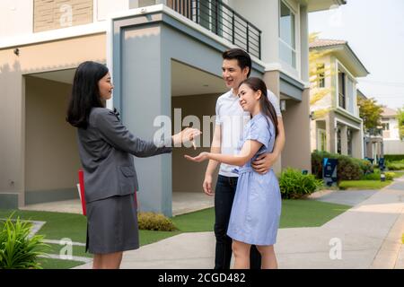 Asiatisches Lächeln junge Paare nehmen Schlüssel neues großes Haus von Immobilienmakler oder -Immobilienmakler vor ihrem Haus, nachdem sie Vertrag unterzeichnet haben, Con Stockfoto