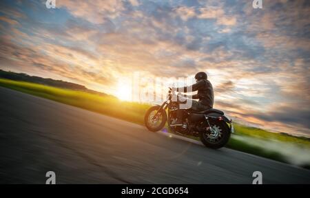 Dunkle Motorradfahrer Reiten High Power Motorrad in der Natur mit schönen Sonnenuntergang Licht. Reisen und Transport. Freiheit beim Motorradfahren Stockfoto