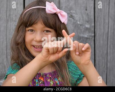 Niedliches gemischtes Mädchen (Ostasiatisch / Kaukasisch) zeigt mit beiden Händen das chinesische Handzeichen für die Nummer 10 (Fotoserie: Bildnr 10 von 10). Stockfoto