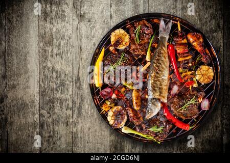 Blick von oben auf frische Rindersteaks, Hühnerschenkel, Fisch, Spieß, Wurst und Gemüse auf dem Grill auf Holzboden platziert. Grill-, Grill- und Food-Konzept Stockfoto