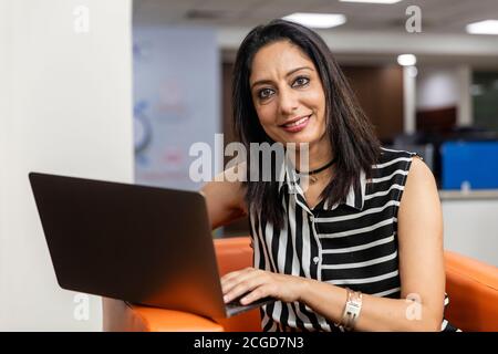 Porträt der erfolgreichen indischen Geschäftsfrau sitzen auf einer Couch und arbeiten auf Laptop, Corporate Environment. Stockfoto