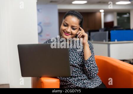 Porträt der erfolgreichen indischen Geschäftsfrau sitzen auf einer Couch und arbeiten auf Laptop, Corporate Umwelt, expressives Gesicht. Stockfoto