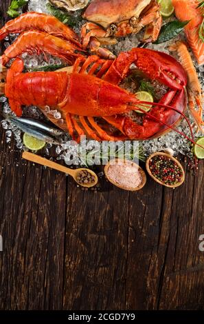Hummer mit Meeresfrüchten, Krabben, Muscheln, Garnelen, Fisch und anderen Muscheln auf zerkleinertem Eis und Holztisch serviert Stockfoto