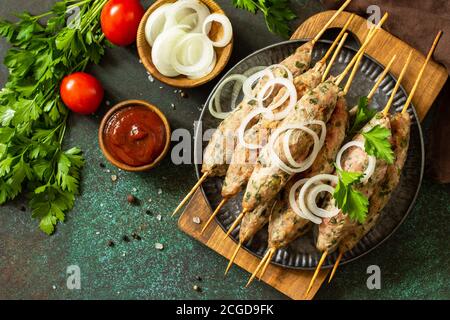 Türkische Kebab. Selbstgemachte Kofta-Kebabs auf einem Spieß mit Gemüse und Sauce auf Stein- oder Schiefergrund. Draufsicht flach lagen Hintergrund. Stockfoto