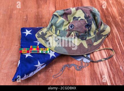 Vietnam Veteran Camouflage Hut, Dog Tags, Service Ribbons & Gefaltete Amerikanische Flagge Stockfoto