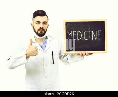 Behandlung und medizinische Genesung Konzept. Arzt mit Bart hält Tafel mit Wort Medizin und zeigt Daumen nach oben. Mann mit selbstbewussten Gesicht in weißem medizinischen Kleid isoliert auf weißem Hintergrund Stockfoto